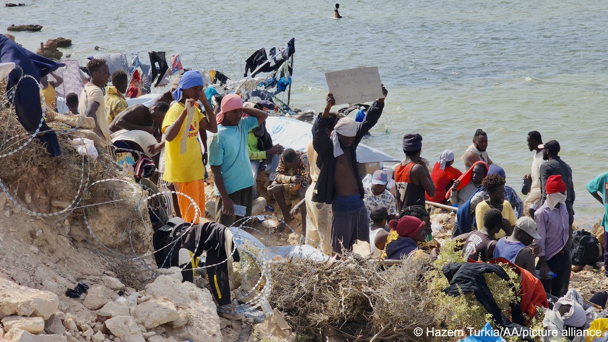 InfoMigrants's tweet photo. 📷 These migrants are stuck at the Tunisian-Libyan border. 

They were forced into the border region by Tunisian forces, and Libyan border guards reportedly won’t let them cross. 

Now, they are living in a makeshift camp in Ras Ajdir next to the barbed-wire border fence. https://t.co/hzmcr6GUfs
