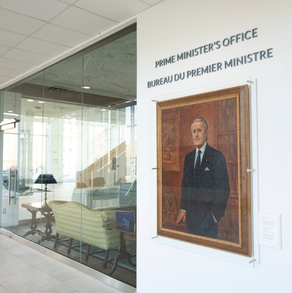 A portrait of the Rt. Hon. Brian Mulroney hangs on a white wall outside the replica of his office in Mulroney Hall. 