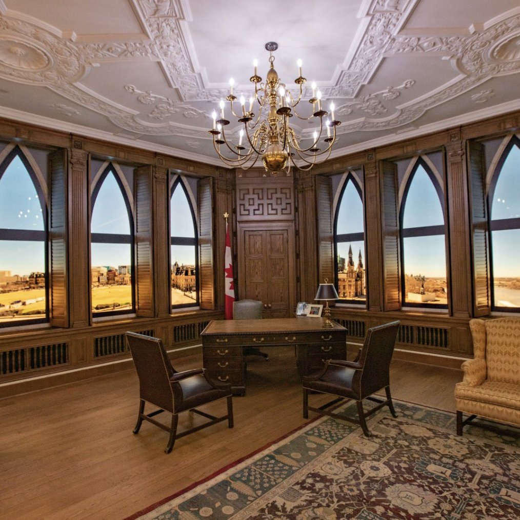A photo of the replica of the Rt. Hon. Brian Mulroney's replica office in Mulroney Hall. It features dark wooden desk and chairs, and a gold chandalier.