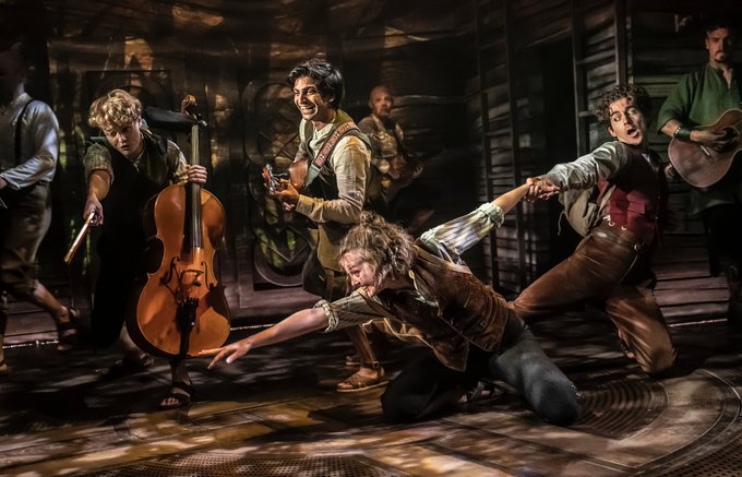 Actor-musicians leap towards something on the floor 