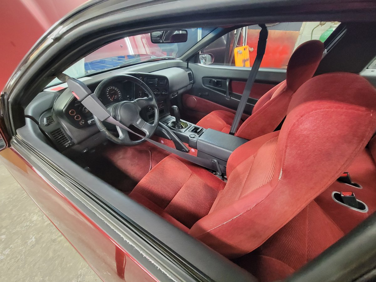 A maroon 1992 Plymouth Laser with the hood up and the red velour interior with automatic seatbelts