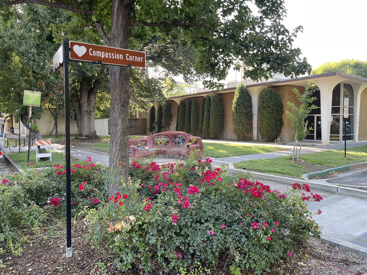 A sign on the corner of 3rd and C Street in Davis that says “Compassion Corner” with the Compassion bench in the background.