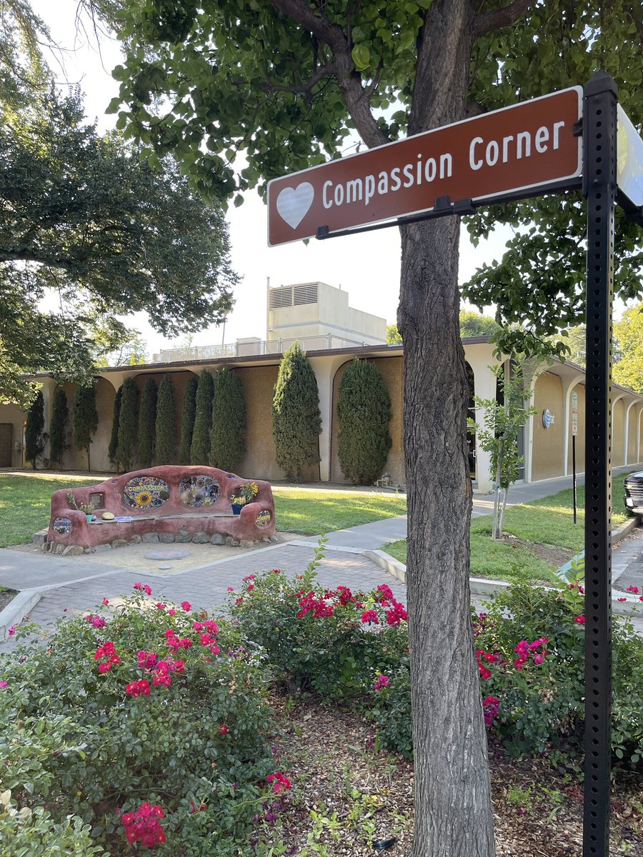 A sign on the corner of 3rd and C Street in Davis that says “Compassion Corner” with the Compassion bench in the background.