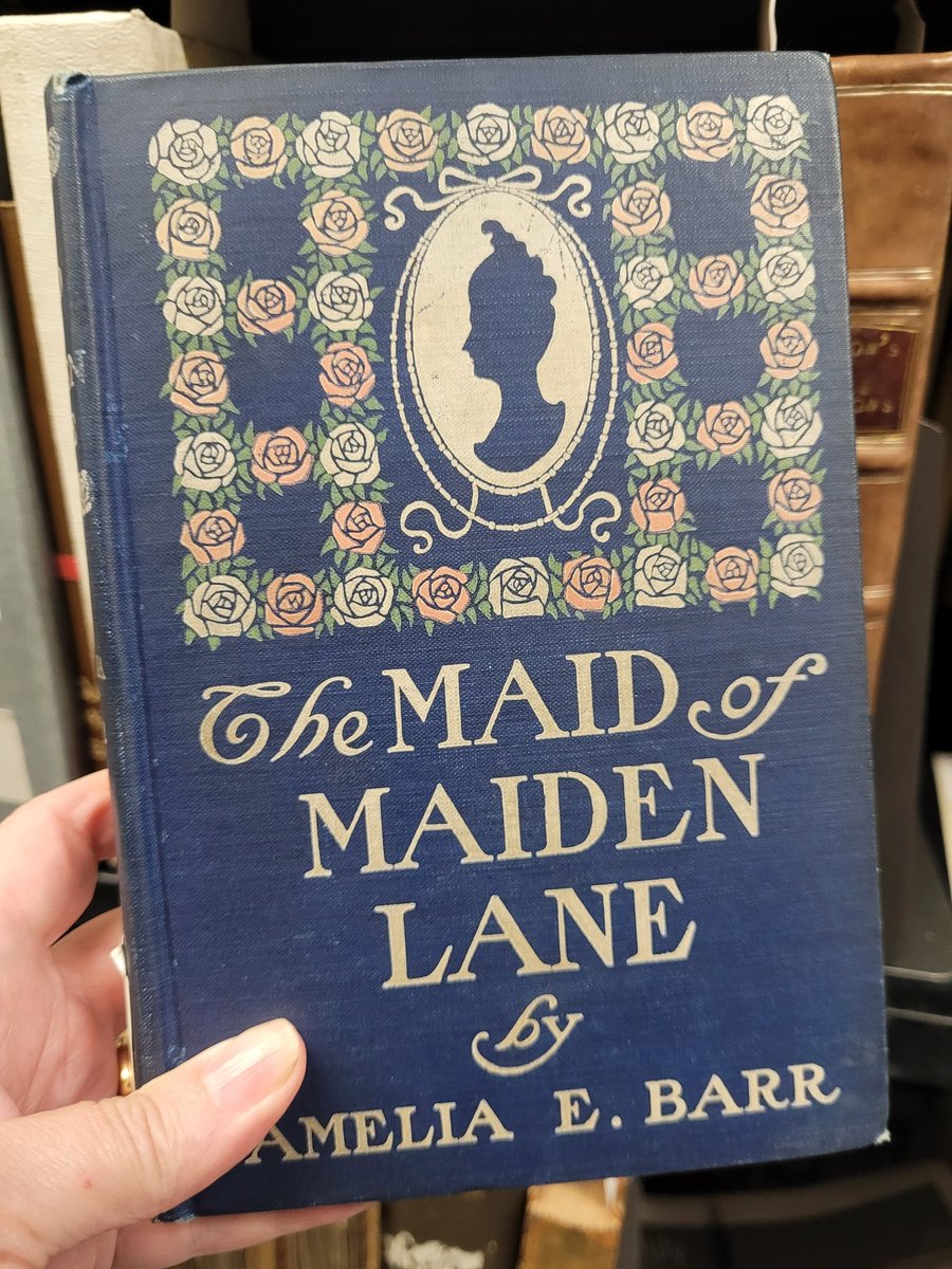 jordan_library's tweet photo. This #PublishersBinding features dark blue cloth stamped in pink, cream, and green with a floral grid surrounding a cream silhouette cameo. Published in 1900, The Maid of Maiden Lane was written by Amelia Barr (1831-1919) and illustrated by S.M. Arthurs. https://t.co/Vm96D8bBXU