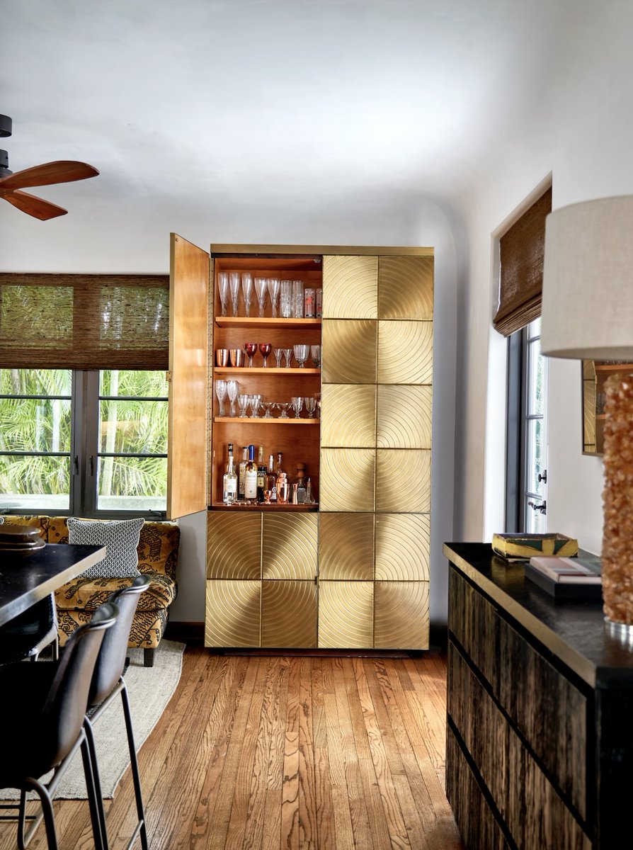 The golden bar cabinet in this Miami home adds a special touch to the warm space. Metal finish are classically neutral but bold and can elevate a design. A bar cabinet should be well-stocked with a variety of glassware.