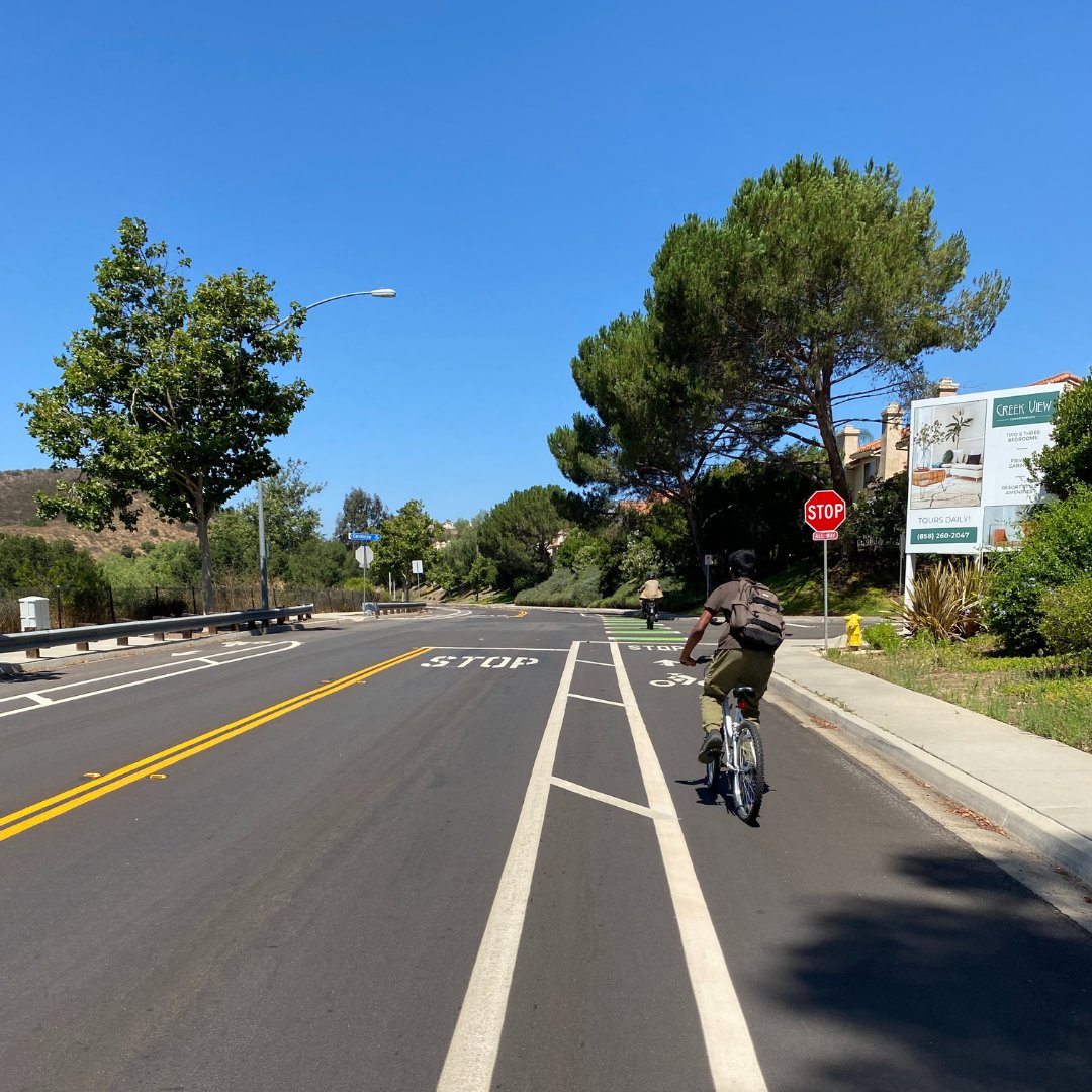 CityofSanDiego's tweet photo. Segment by segment, Sabre Springs Parkway is being slurried & striped! Cyclists & other micromobility riders can count on a smooth roadway surface, newly striped buffered bike lanes and green-colored crossings to increase safety and visibility while out for a ride. #FridayRoadFix https://t.co/zzNNRq0B9X