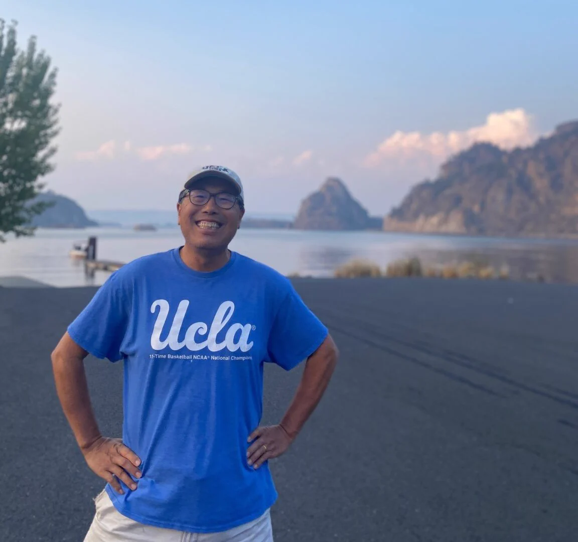 Professor An Yin wearing a blue UCLA shirt and smiling in front of a lake in Eastern Washington.