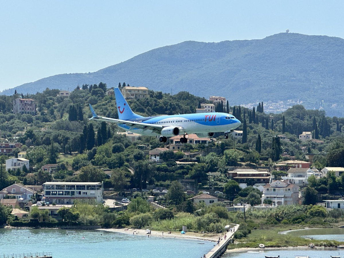 A TUI 737 landing in Corfu with sea below and a hillside with some buildings in the distance.