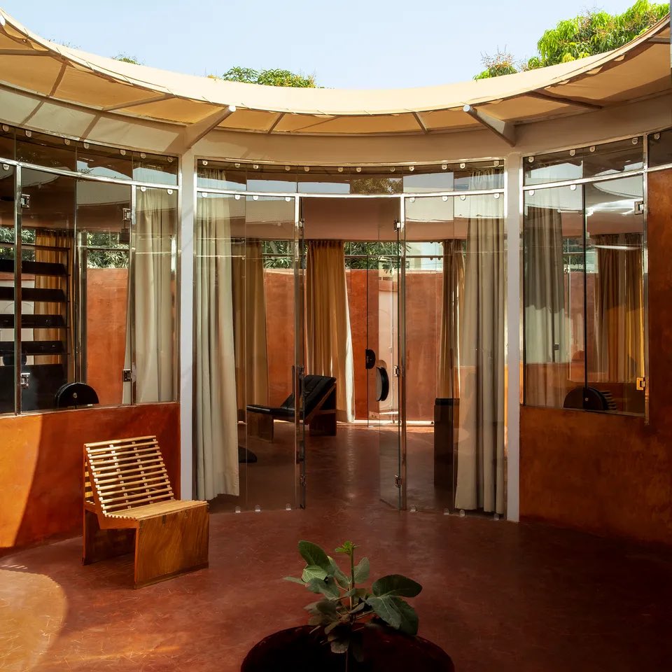 iam_blacklegacy's tweet photo. Coup de cœur architectural au Sénégal 🇸🇳 : La villa minimale du mannequin Malick Bodian

À Ngaparou, au sud de Dakar, la Villa Aram est une construction artisanale inspirée. Cette réalisation bioclimatique à la fois humble et contemporaine allie techniques traditionnelles et matériaux hérités du minimalisme du XXe siècle.

Le terrain n’est pas très grand (300 mètres carrés), enserré dans le tissu urbain dense mais parsemé de manguiers de Ngaparou. La villa, construite pour le mannequin et photographe Malick Bodian, possède un dessin affirmé au style minimal et doit répondre aux besoins de confort et d’usage propres à une maison de famille. 

Son inspiration, l’architecte Cyrus Ardalan l’a puisée dans les constructions traditionnelles du Sénégal, privilégiant l’utilisation de matériaux de proximité. Un projet total qui met en valeur l’artisanat et repense la manière de construire, en s’imprégnant de l’esprit local. 

Je cite : « Mon point de départ a été la case à impluvium de Casamance, avec son plan radial et son arbre qui pousse au milieu. Je l’ai modernisée en prenant pour référence le travail de l’architecte Glenn Murcutt : les Australiens sont les pionniers de la construction responsable, qui s’extrait de toute climatisation et autres procédés énergivores... »

Les espaces se caractérisent par leurs nuances de rouge et de corail, sublimées par l’usage de verre et d’Inox poli miroir. Le mobilier, parfois intégré, est dessiné par Cyrus Ardalan. Chaises et fauteuils comportent différents types de profils d’assise ainsi qu’un revêtement en cuir pour l’intérieur ou la possibilité d’être repliables pour la piscine. Les rideaux en coton naturel permettent de voiler les façades vitrées créant une seconde atmosphère plus claire. Au centre, un figuier donnera encore plus de fraîcheur aux chambres.

La Villa Aram propose une ambiance colorée, due à l’utilisation de terre crue et de terre cuite, sourcées à proximité. Le dimb, un bois endogène du Sénégal, teinté ou naturel, est à l’origine des portes et du mobilier dessinés par l’architecte et réalisés par des artisans locaux.

(Source : Architectural Digest France)