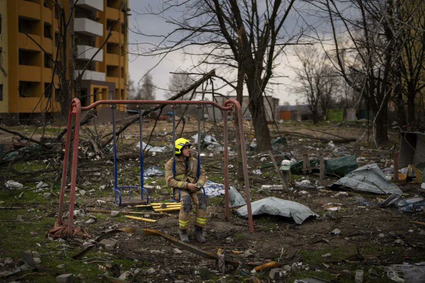 A firefighter sits on a swing next to a building destroyed by a Russian bomb in Chernihiv, Ukraine in April 2022 (Emilio Morenatti/AP)