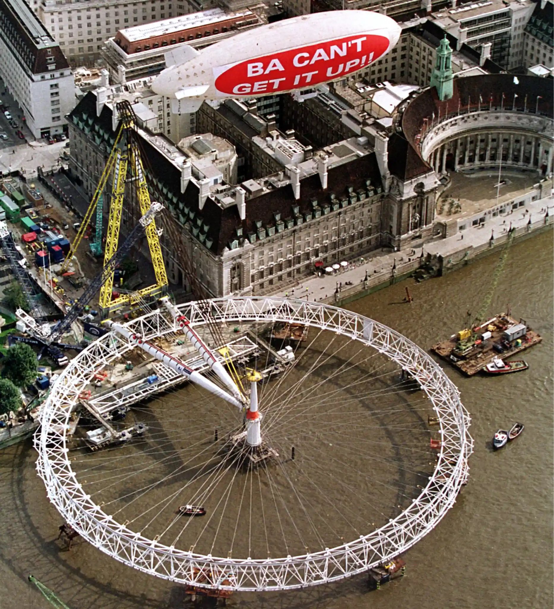 blimp over the disassembled London Eye with a bold white caption “BA CAN’T GET IT UP!!” over red background