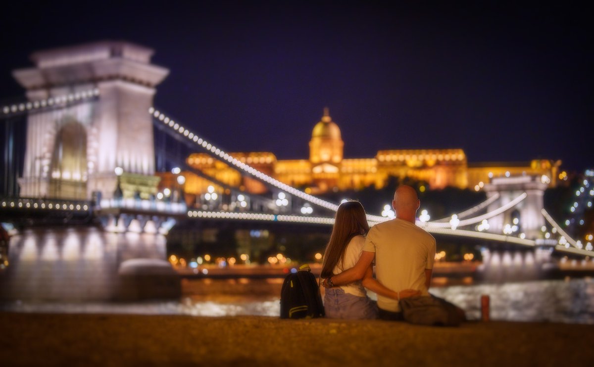 Budapest, Hungry, a couple embrace while looking over the Danube River toward the Budavari Palota (Buda Castle) and the Széchenyi Chain Bridge. #Sony50mmGM #SonyLens SonyAlpha #Alpha1 #bealpha #sonyphotographer #danuberiver #europe #castle #lighting #travel #building #cityscape