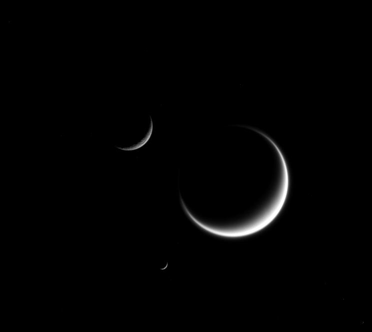 Titan, the largest moon in this image, appears fuzzy because we only see its cloud layers. And because Titan's atmosphere refracts light around the moon, its crescent "wraps" just a little further around the moon than it would on an airless body. Rhea (upper left) appears rough because its icy surface is heavily cratered. And a close inspection of Mimas (center bottom), though difficult to see at this scale, shows surface irregularities due to its own violent history. The image was taken in visible light with the Cassini spacecraft narrow-angle camera at a distance of approximately 2.7 million miles (4.3 million kilometers) from Titan. 

Image credit: NASA/JPL-Caltech/Space Science Institute