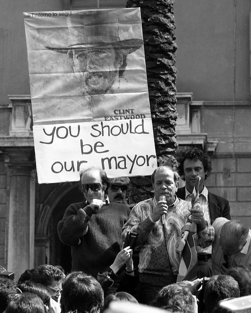 CrazyItalianPol's tweet photo. Comedians Giorgio Bracardi and Bombolo, together with Communist Party deputy Renato Nicolini, participate in the 1986 anti-fast food demonstration to protest against the opening of the McDonald's restaurant in Piazza di Spagna, Rome. 

The sign behind them, celebrating the American actor Clint Eastwood, was due to the fact that he, who had just that year become mayor of the Californian city of Carmel-by-the-sea, had banned the opening of a fast food restaurant.

Sub by @f_bartoloni