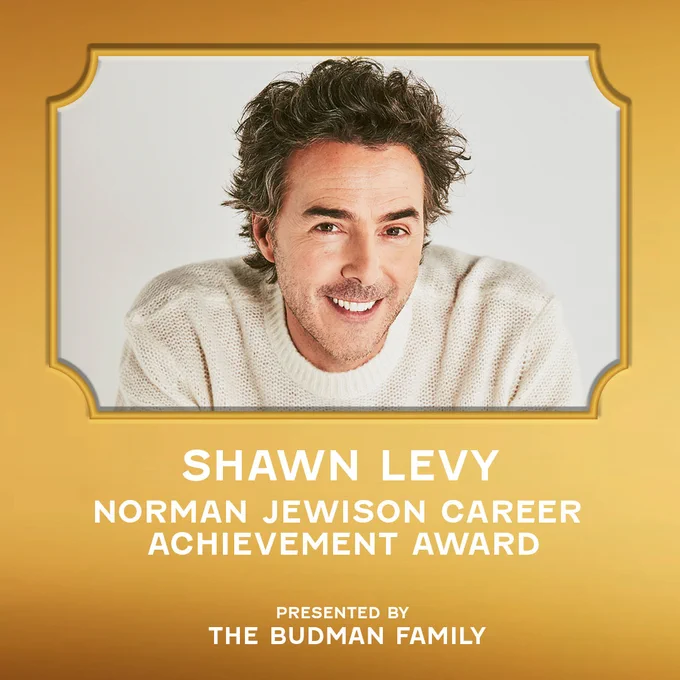 A golden design asset featuring a photo of Shawn Levy. He is sitting with his arms resting on his legs, wearing a white sweater with the sleeves pulled up, posing against a white background. The text reads “Shawn Levy, Norman Jewison Career Achievement Award, presented by The Budman Family”.