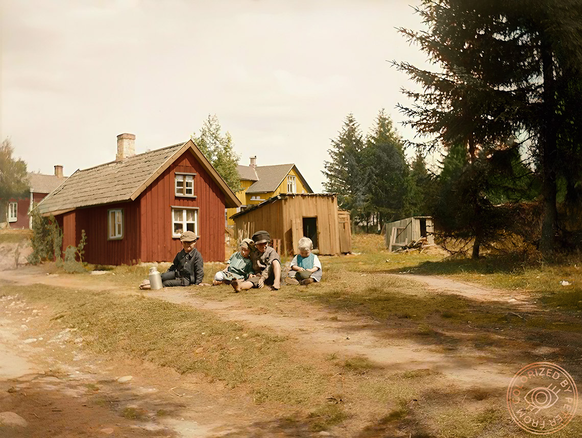 Lekande barn vid öppen gräsmark, invid dem ett mjölkkrus. I bakgrunden trähus. Någonstans i Ed anno 1913. Kolorerad av mig. RT:a gärna så att fler får ta del av vår vardagshistoria. 🇸🇪❤️