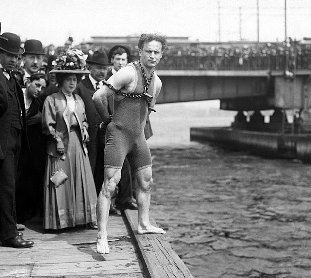 historyinmemes's tweet photo. In 1908, Houdini found himself on the Harvard Bridge, often known as the Mass. Ave. Bridge, where he was restrained by a Boston patrolman. His hands were securely handcuffed behind his back, connected by chains to a collar around his neck. Over 20,000 spectators gathered to witness his daring leap.

Houdini performed this stunt just two weeks before an upcoming show in Boston, using it as a promotional spectacle. The "Impossible Possible" maestro aimed to elevate his reputation for escaping handcuffs and chains by attempting the feat underwater. As reported in a Boston Globe article, a signal sounded from a towboat, prompting Houdini to plunge into the chilly waters below.

The onlookers anxiously waited for 40 seconds until the magician resurfaced, triumphant, holding the liberated shackles in his hands.