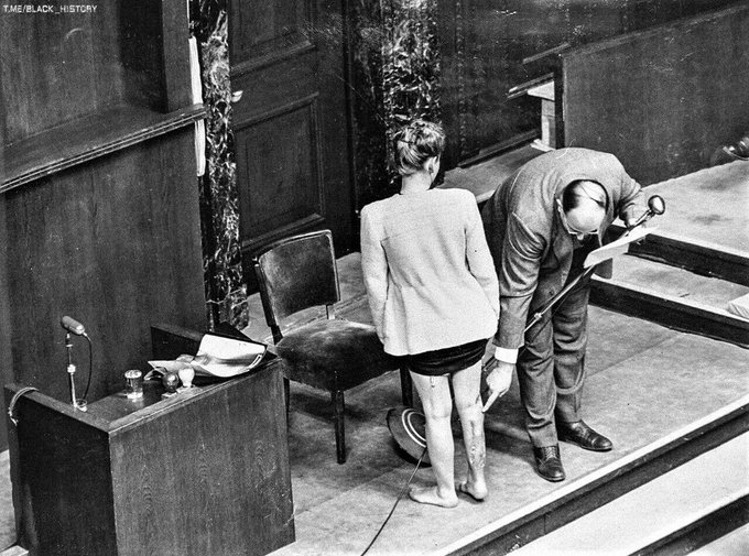 A former prisoner of the Nazi concentration camp Ravensbrück demonstrates traces of bullying at the Nuremberg trials in the presence of a doctor giving an explanation, 1946.