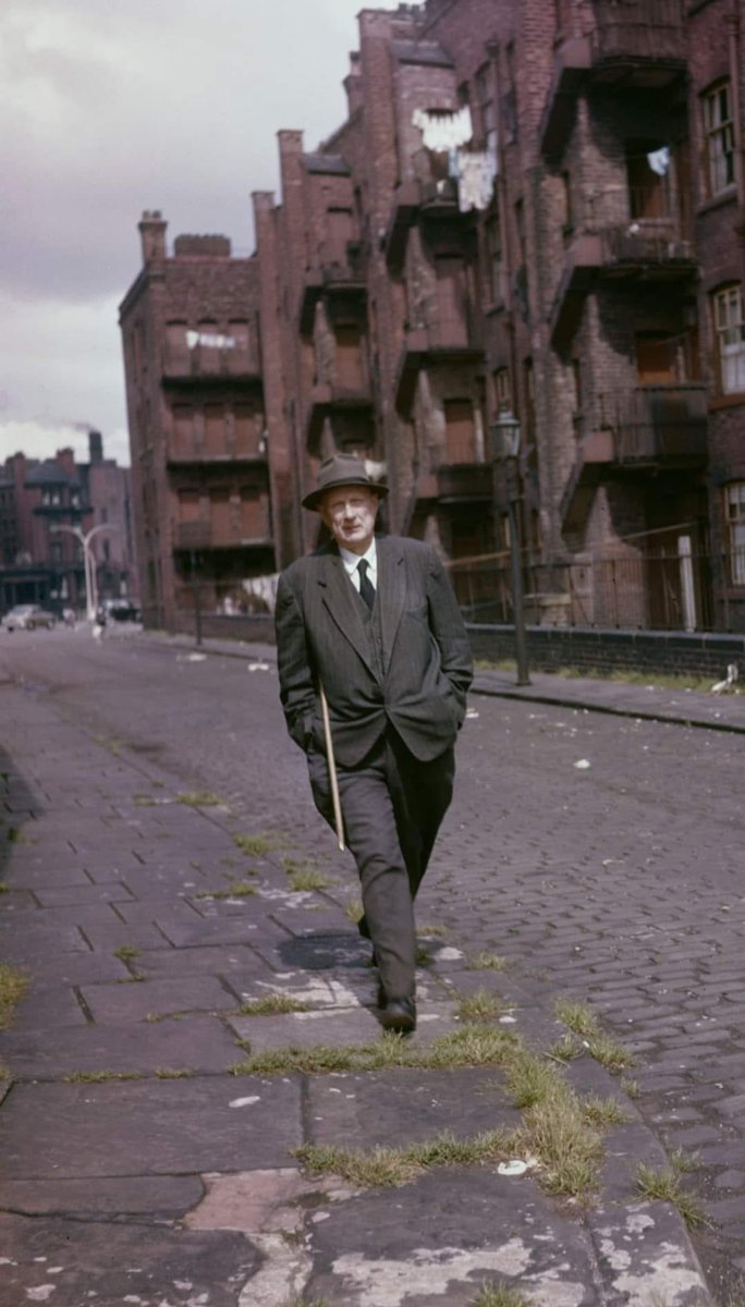 L.S. Lowry walking through the back streets of Salford, August 1957. In the background are Oldfield Road Dwellings.