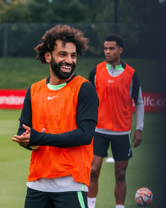 Mo Salah smiling in training, with Cody Gakpo visible in the background.