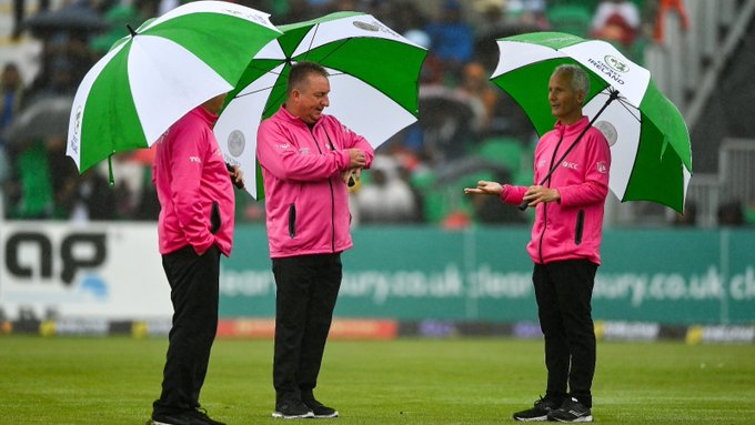 Three match officials with umbrellas hold a discussion on the outfield ahead of the third Ireland-India T20I