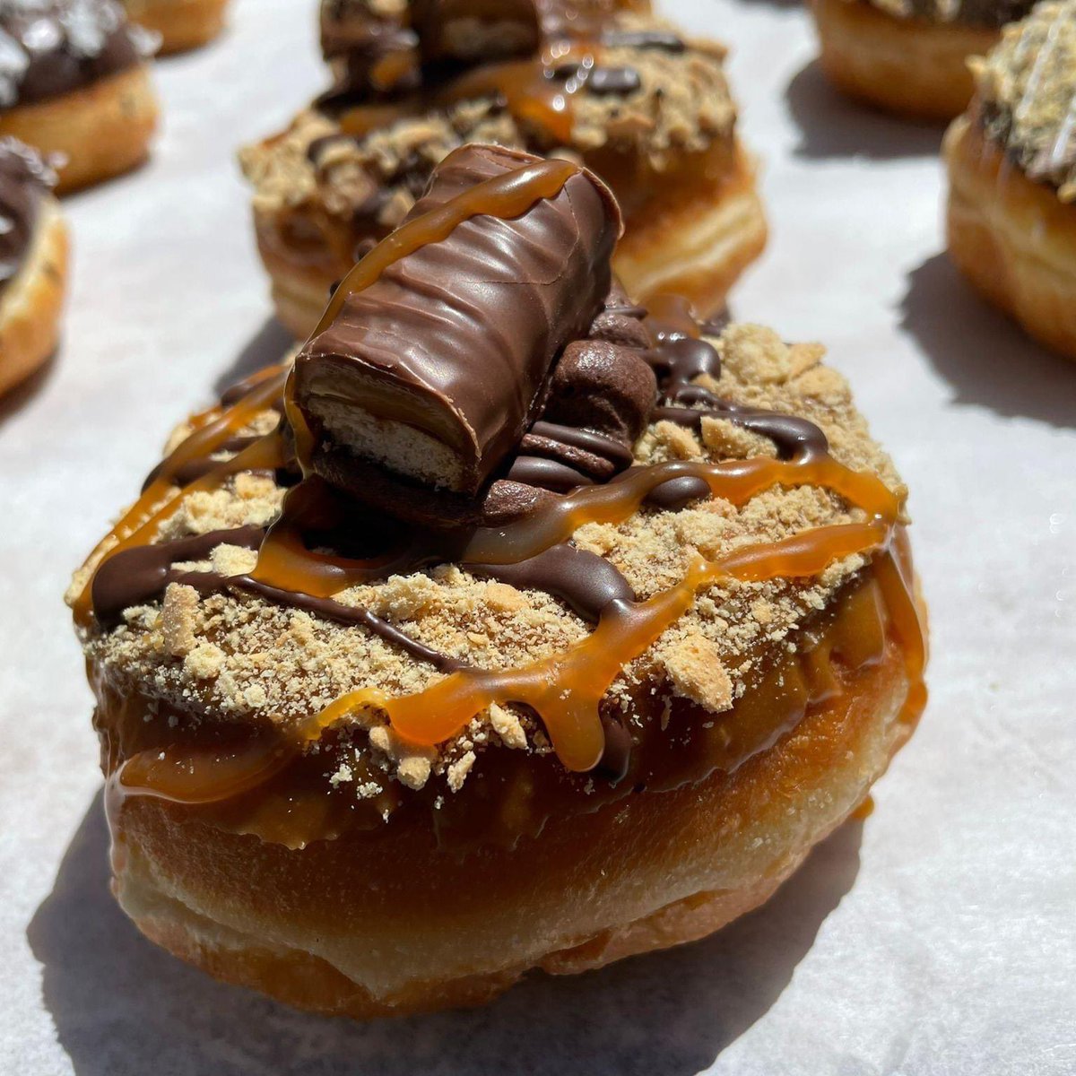 You DOUGHNUT want to miss this! Kick off the long weekend with a trip to the bakery and treat yourself to our Caramel and chocolate doughnut topped with Twix. #summerofdoughnuts #doughnuts #donut #twix