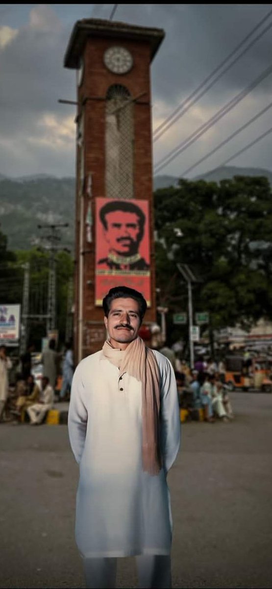 An AI-generated image depicts the martyr Maqbool Butt Sahib standing near Upper Adda Chowk.Technology used in the image brings attention to the remarkable resemblance between the Kashmiri martyred leader and the poster behind him..!