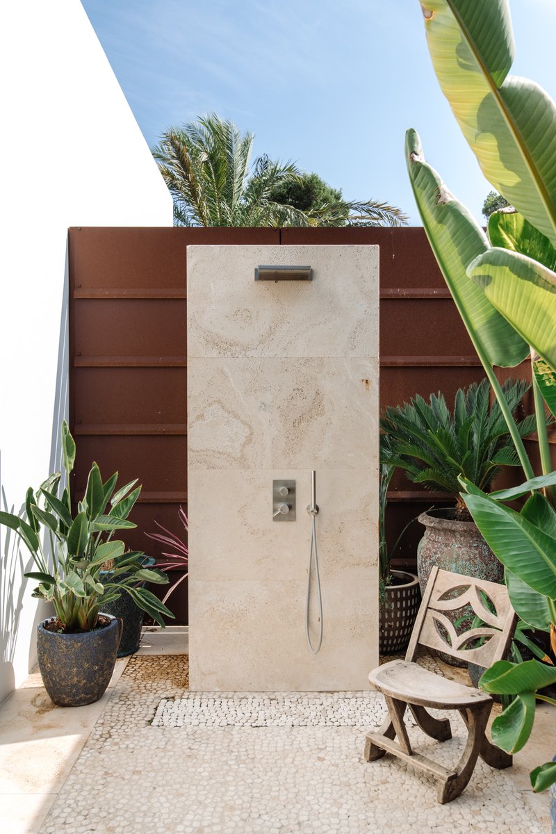 I love an outdoor shower, especially when nestled in greenery and made of natural materials. The creamy travertine contrasts with the oxidized metals walls. The vintage folding chair adds a rustic touch.