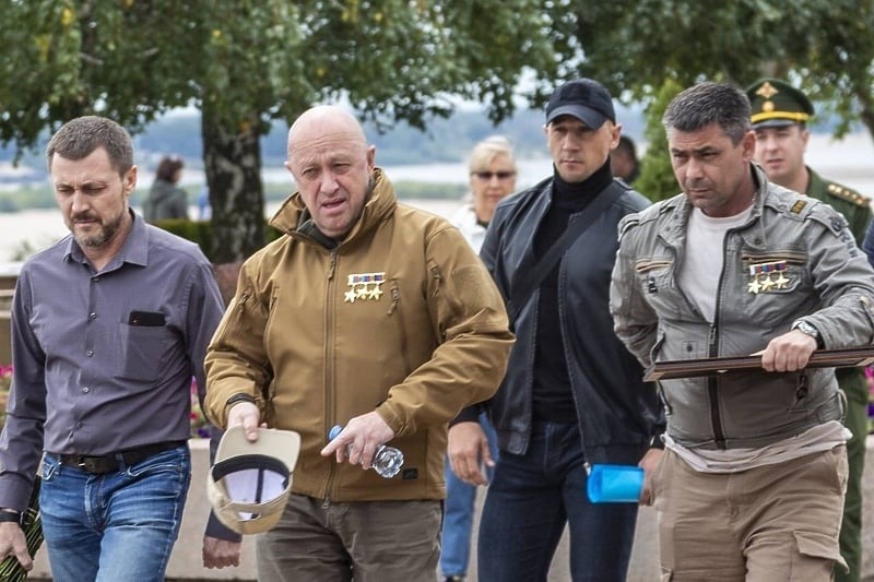 christogrozev's tweet photo. .@Dobrokhotov and I did some deep reverse face search for this face, and discovered that he was most likely Prigozhin's personal bodyguard.  Here, he is walking behind Prigo in black cap. Thus, if the bodyguard was on board, the overwhelming chances are Prigozhin was there too. https://t.co/3aBJ1YXm6A