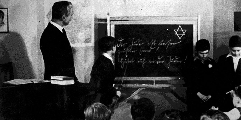 Initially, Jewish children used to go to the same schools as other German children. The Year was 1930 . These two Jewish children are being humiliated in front of the whole classroom. The text on the blackboard reads.... 'The Jews are our greatest enemy !! Beware of Jews. !! '…