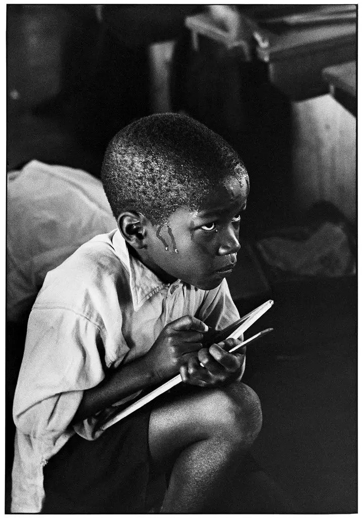“Boy in School”
A boy clutches a chalkboard in an overheated and unfurnished classroom.