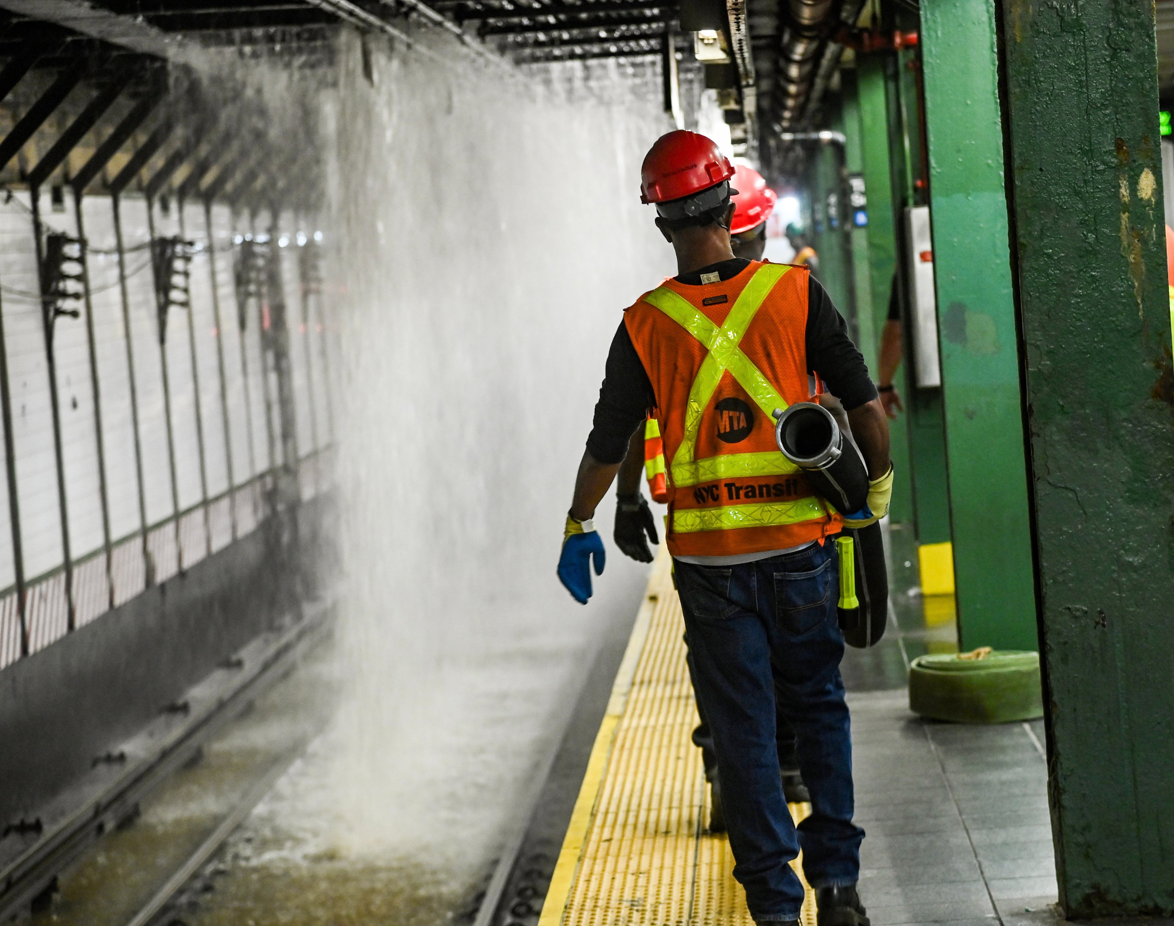 Crews carrying a pump hose on the platform at Times Sq-42 St station in response to water pouring onto the tracks.