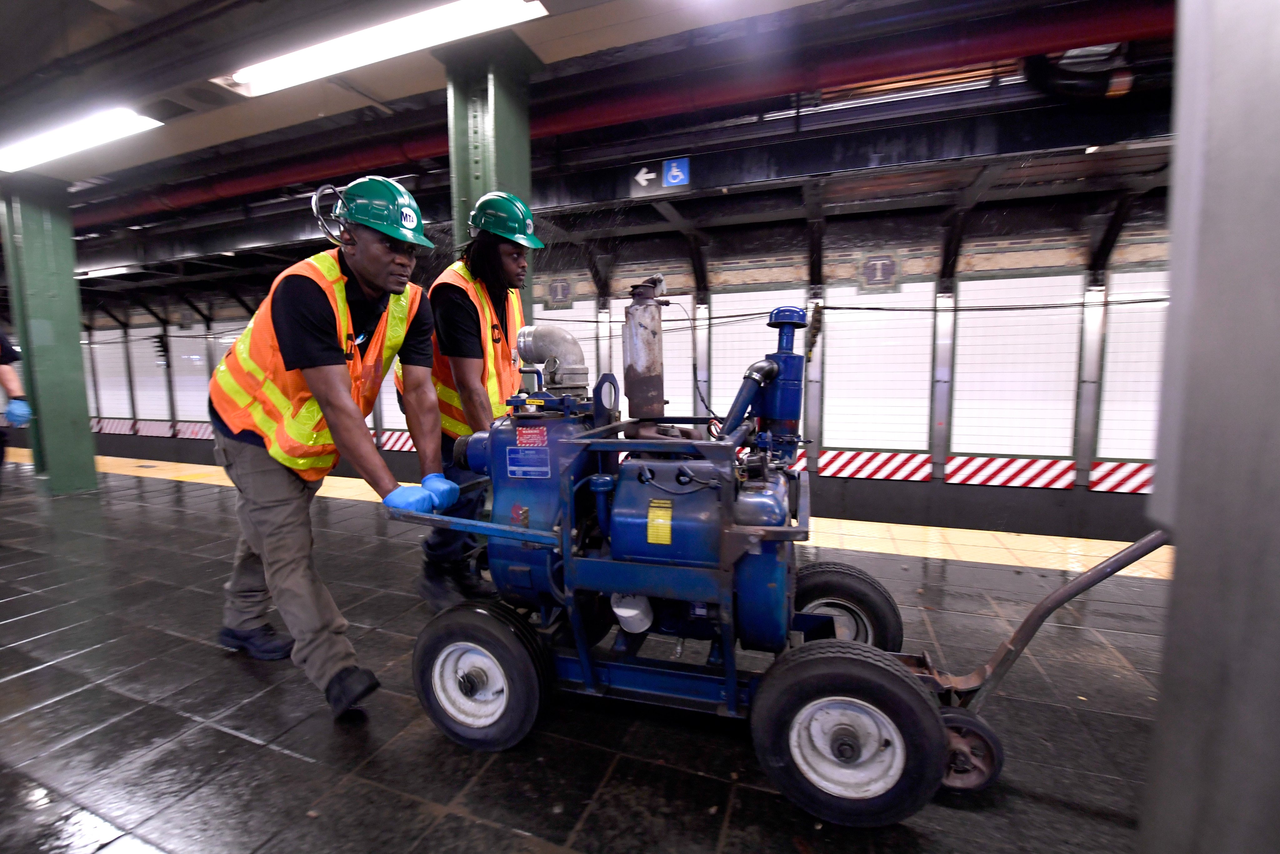 Crews maneuvering a blue water pump motor on the platform at Times Sq-42 St station in response to water pouring onto the tracks.