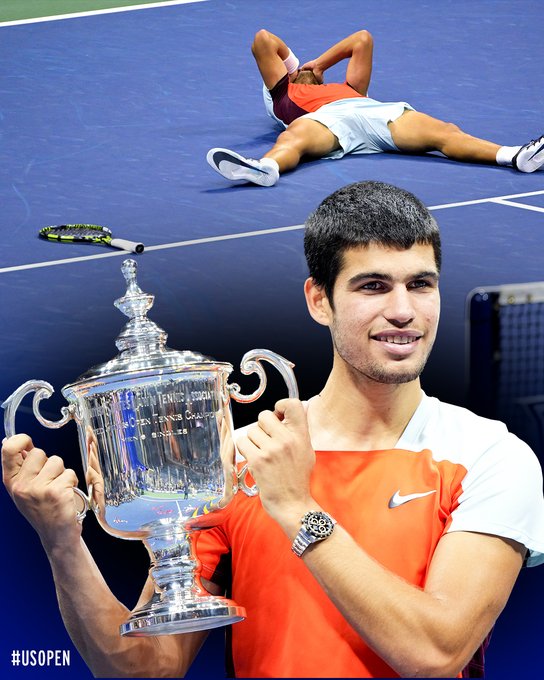 Photo of Carlos Alcaraz holding the 2022 US Open trophy and laying on the court. 