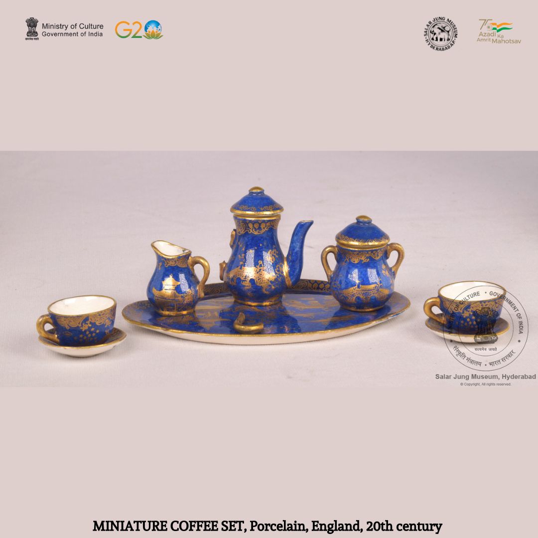 Miniature coffee set from England, dated 20th century. Chinese subjects are painted in gold over the blue porcelain surface of this set consisting one oblong tray, two cups, an saucer, one coffee pot, one milk jug and one sugar pot. 
#SalarJungMuseum #AmritMahotsav #coffeeset