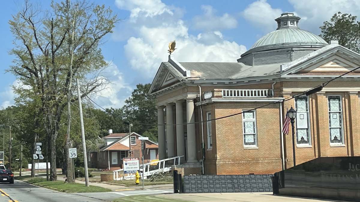 JMichaelBrewer's tweet photo. Since there has been some conversation this week about the cleanup work going on at the Old First Baptist Church in Jackson, GA, here is some historical information about the building that you might find interesting. 

The building was constructed on East Third Street, adjacent to its predecessor that was later torn down for the church parking lot on the east side of the building. The church building program, which was planned for several years, was led under the pastoral leadership of Dr. Robert Van Deventer, who pastored the First Baptist Church of Jackson for 16 years. The cornerstone was laid on May 22, 1914 and it was completed later that year at a cost of $35,000.00. The membership held their first service in the new building sanctuary on December 20th, 1914. The building is constructed primarily of brick and the original part of the building was 109 feet long by 60 feet wide, with a 35 foot wide loggia or portico supported by four massive columns. Other additions followed decades later. 

The materials used to build the church were sourced from Washington DC (brick), North Carolina (steel roof), Virginia (slate) and of course, Georgia (marble and lumber). The stain glass windows were crafted by the Empire Glass Company in Atlanta and dedicated as memorials to several founding members of the church. Most of the windows remain in place to this day. 

The style of this building is classical Grecian and featured porticos, pediments, doric columns, balustrade railings (removed in recent years) and pilasters. The defining feature of the Old First Baptist Church, which is unique in Butts County, is the monumental domed roof, which is constructed of curving copper panels and crowned with a windowed cupola to allow light to enter at the top. At some point, the dome was painted silver but as the paint has worn away, the oxidized green copper is beginning to show through again. 

At the time of its construction, the building contained basement spaces which held the kitchen, a dining hall, a gymnasium and a concrete swimming pool. The main floor consisted of the sanctuary, which could seat up to 400 people, with Sunday school rooms surrounding the sanctuary on the main level and upper floor which could be opened up when additional seating for worship services was needed. 

When it was completed in 1914, the church was very modern by the standards of the time, featuring electric lighting in all areas of the building (Jackson had only had electricity for a few years in 1914), and indoor plumbing throughout, both installed by the Newton-Carmichael Hardware Company of Jackson. It was heated by a modern furnace system built by the Williamson Heating Company of Atlanta and special care was taken in the design of the building to ensure excellent ventilation during the hotter months of the year. The sanctuary style is known as the Akron plan, which is known for having a central sanctuary surrounded by wedge shaped classrooms that radiated out from the pulpit area. 

The Old First Baptist Church was designed by Sayre & Baldwin Architects and contracted by Quartermus & McDonald Contractors of South Carolina. It was used by the congregation for just over 60 years, from December 20th, 1914 until the final service on July 20th, 1975. The congregation moved into a brand new church on Highway 16 west and the building was sold to the First Assembly of God, who would go on to use it for more than 20 years before it was sold again. As of August 2023, the building is privately owned and is for sale, though no plans have been announced for it as of this writing. 

The black and white photo was made at the time the building was completed and shows both the older original wooden structure next door that was torn down in 1916, two years after the 1914 building was completed. The colorized post card also is from 1914 and shows the copper dome as it would have looked before it weathered green. #ButtsCountyGa #History #JacksonGA #architecture