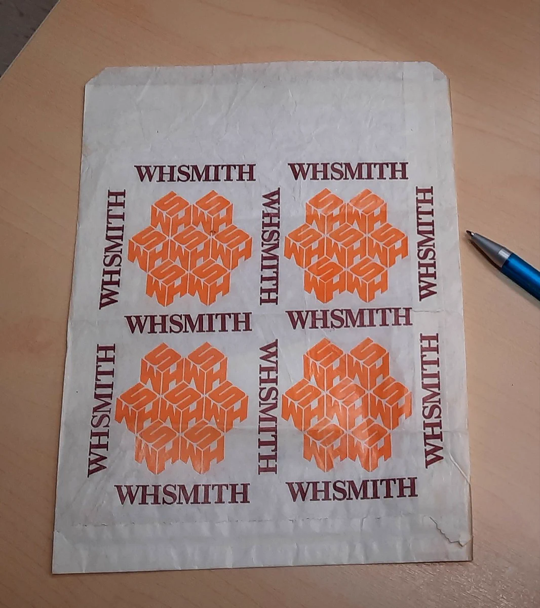 An old white paper bag with a repeated design of the text WH Smith in brown and cubes made up of the letters WHS in orange.
