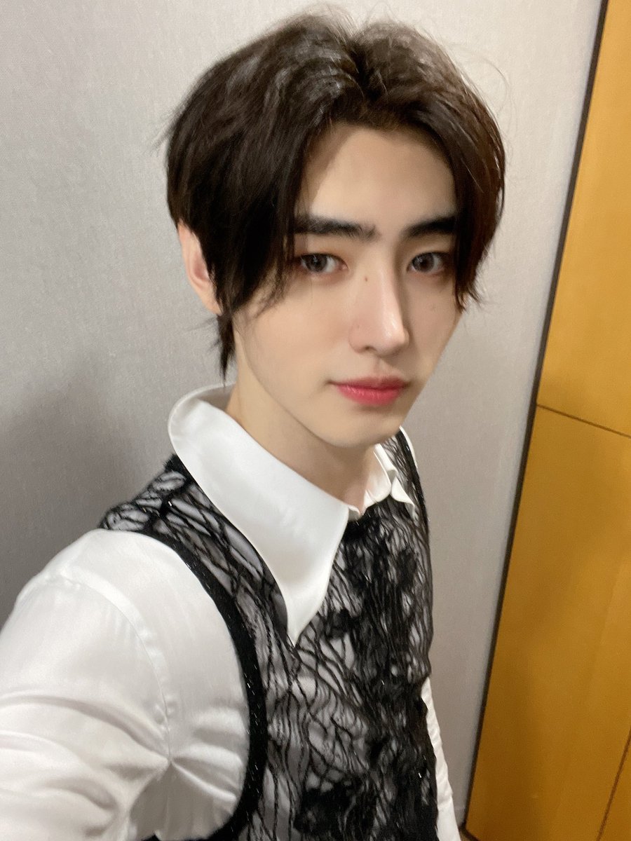 He exudes a chic and self-assured aura, wearing a sleek black vest paired with a crisp ivory shirt. This stylish combination elevates his charisma and sophistication, while the effortless blending of these colors forms a captivating and dynamic presence.
