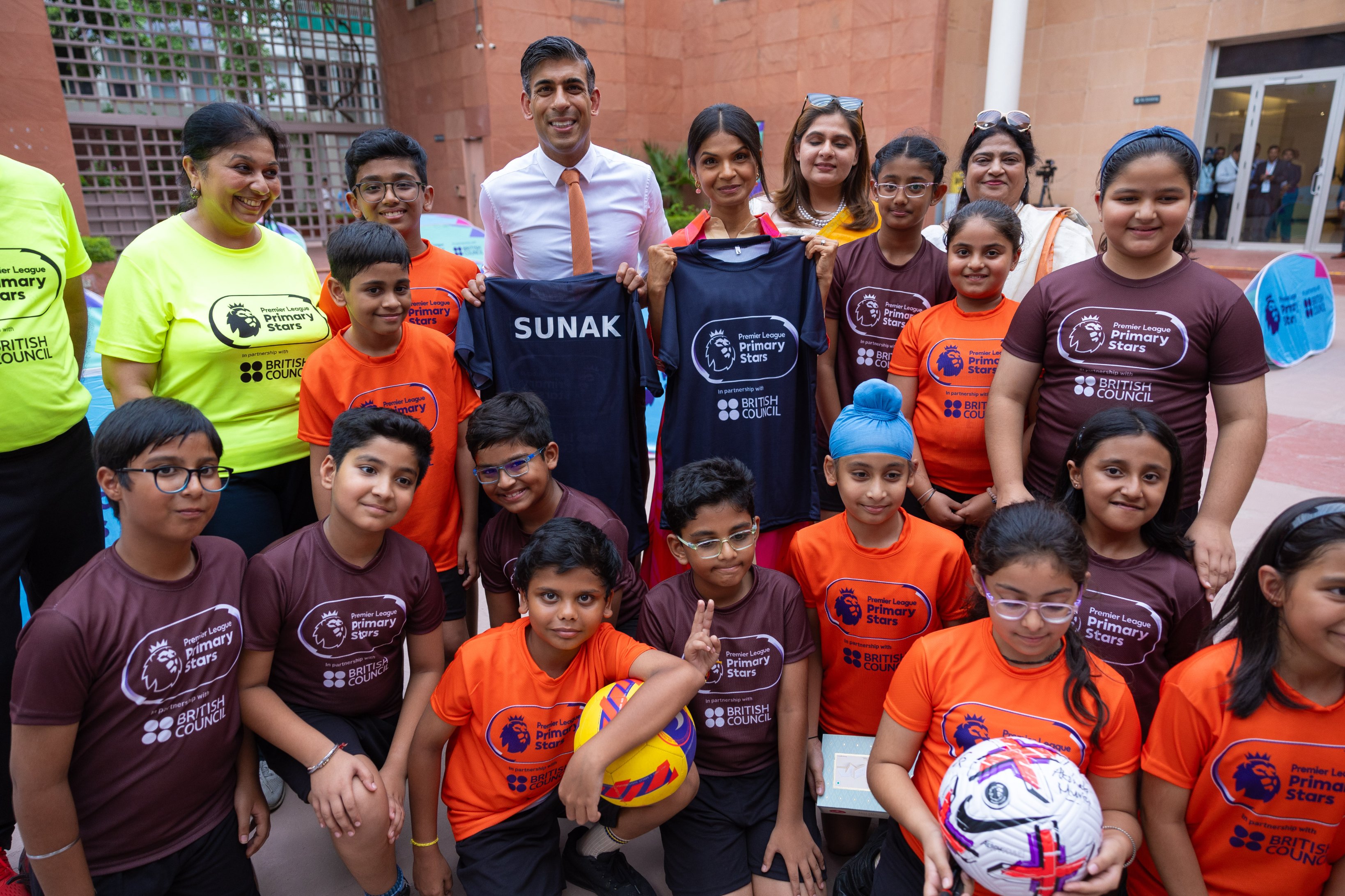 Prime Minister Rishi Sunak and his wife Akshata Murty take a group photo with students at the British Council in Delhi, holding up football shirts. 