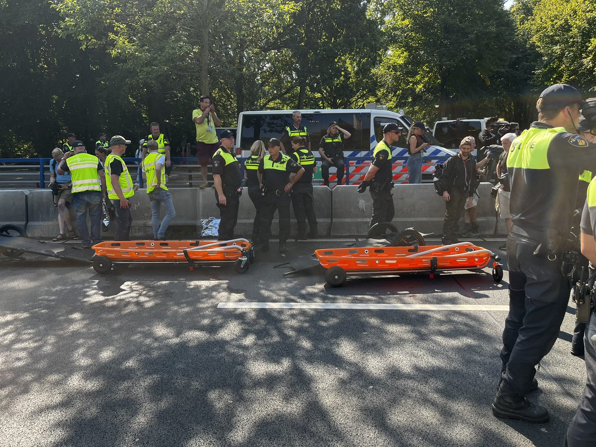 De politie begint elk moment met aanhouden van XR’ers. Touringcar om ze mee af te voeren staat klaar. Net als brancards op wielen om tillen iets makkelijker te maken. Hoe dan ook blijft het fysiek loodzwaar voor de agenten, elke demonstrant los afvoeren. Zeker met deze hitte.