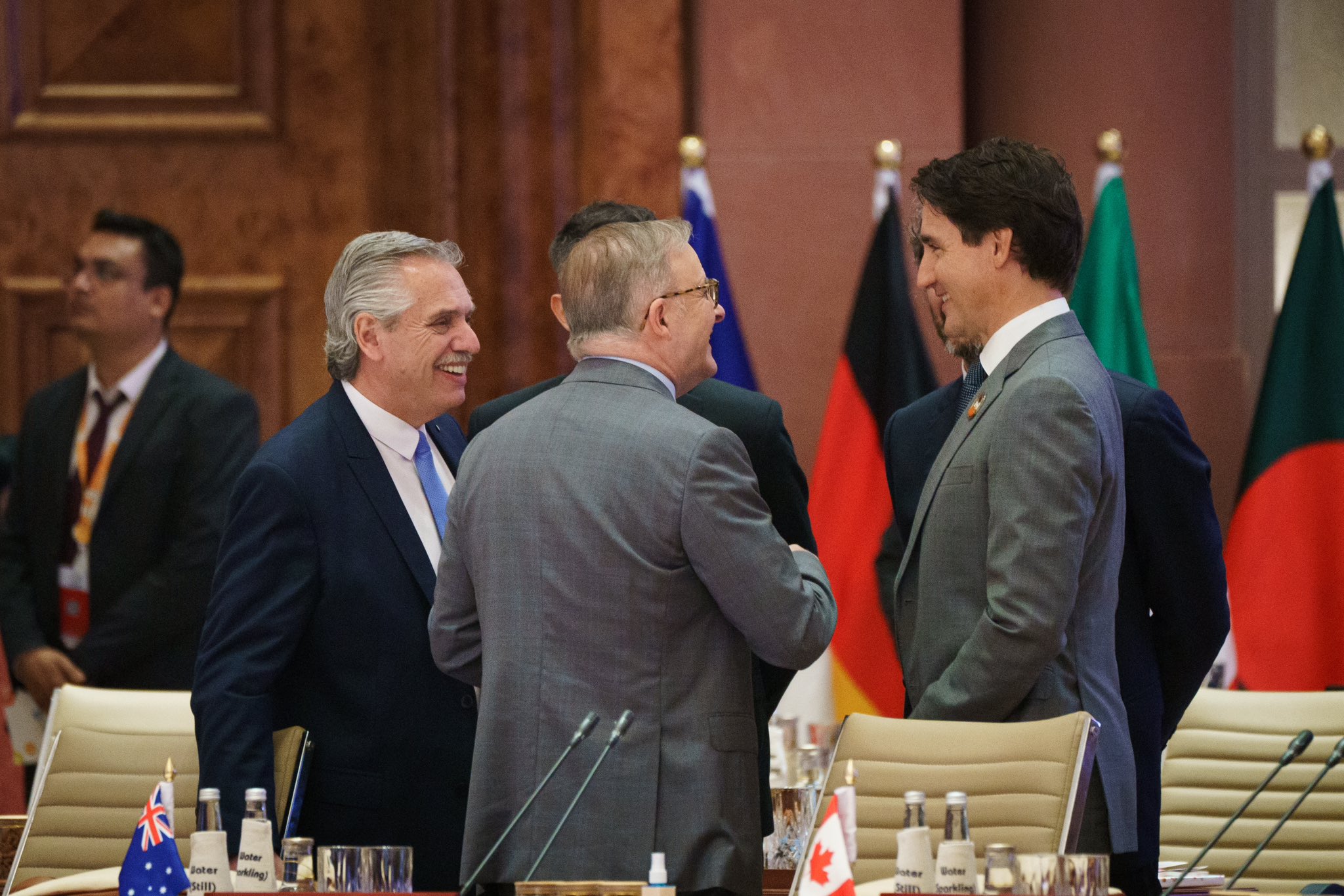 Le premier ministre Justin Trudeau est debout à côté d’une table de conférence et discute avec un groupe de dirigeants. Ils sourient. Une rangée de drapeaux se trouve derrière eux.
