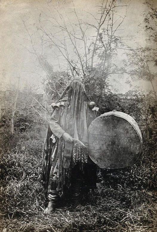 A shaman in ceremonial dress and covered face. Siberia, c1915