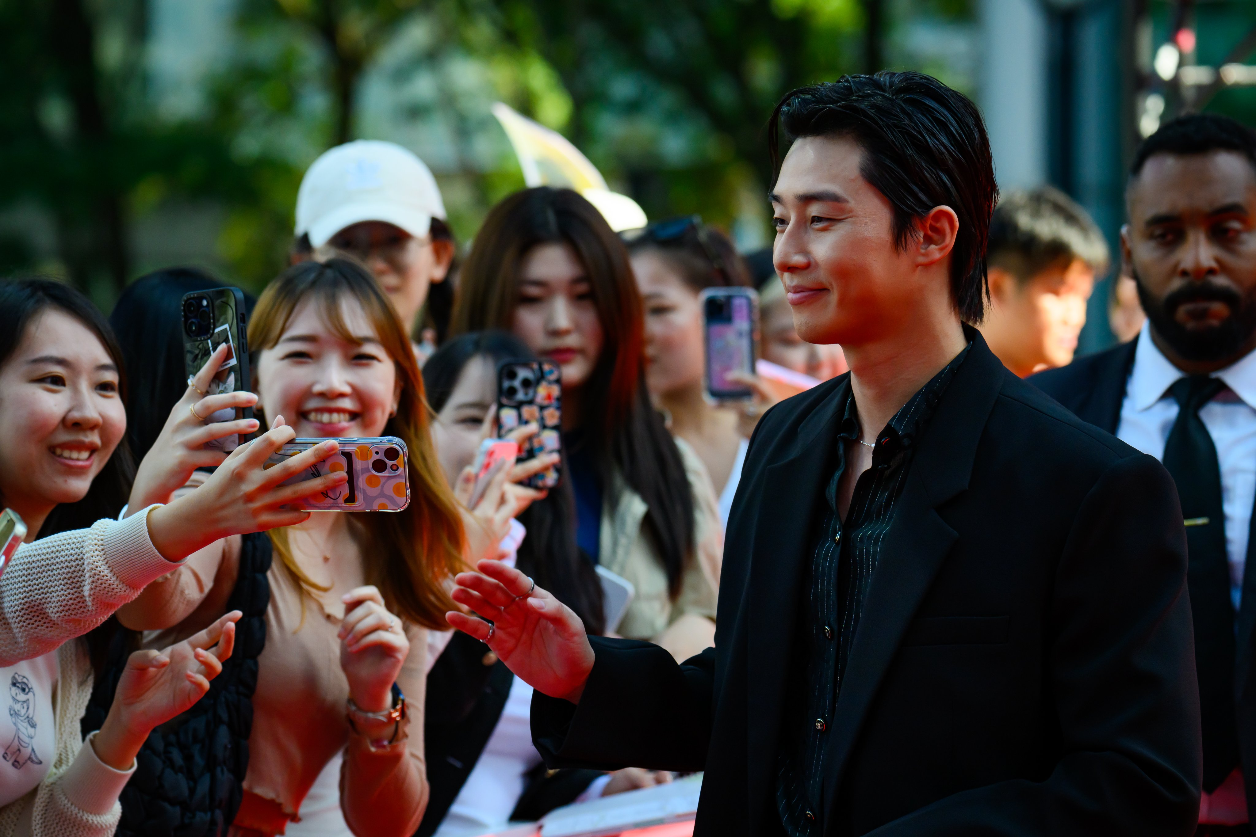 Park Seo-jun smiling and waving with fans behind him, all holding phones up and smiling. 