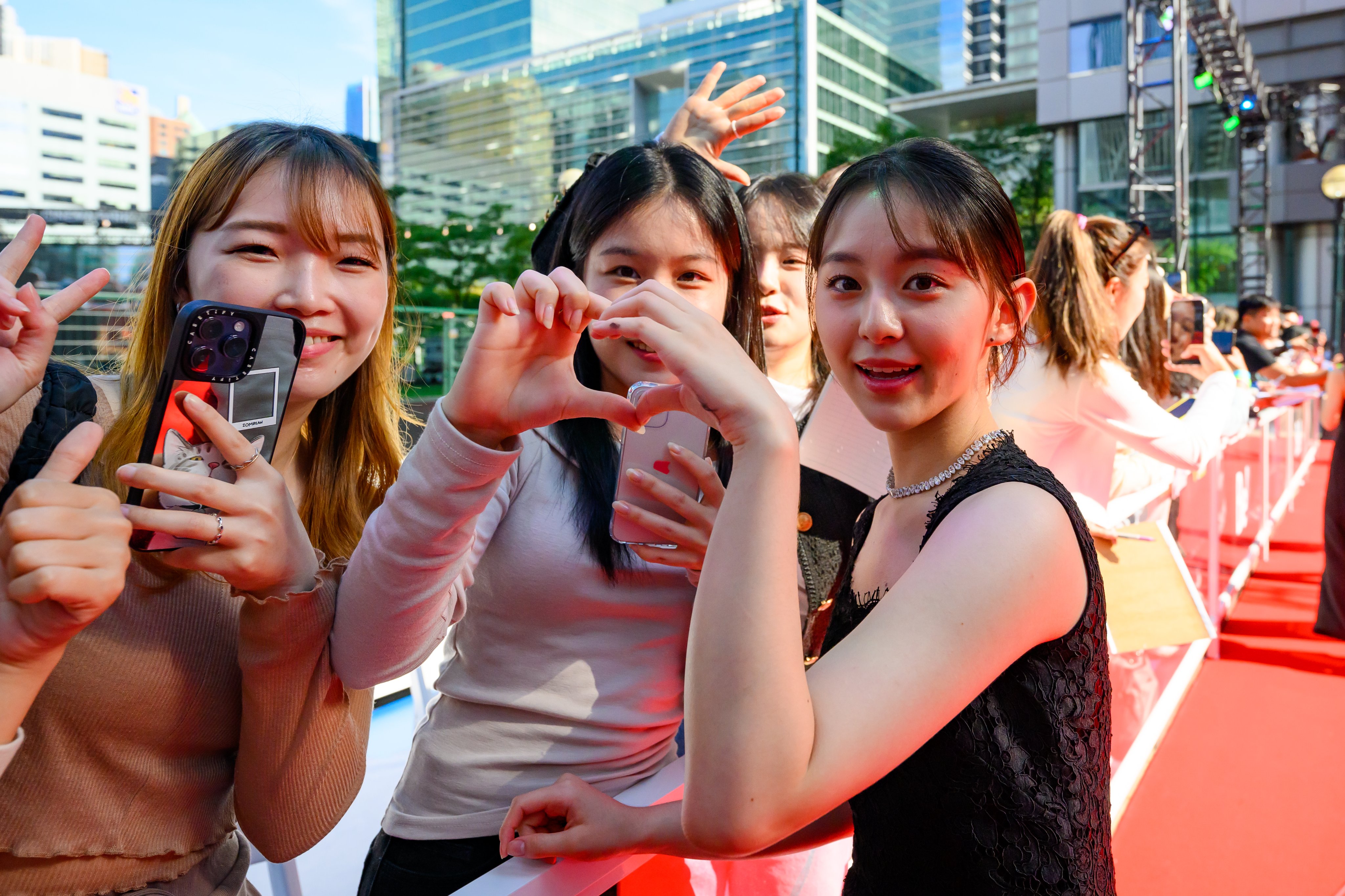 Park Ji-hu smiling and posing with a fan. She has her left hand up to the fans hand and they create a heart shape with their hands together. 