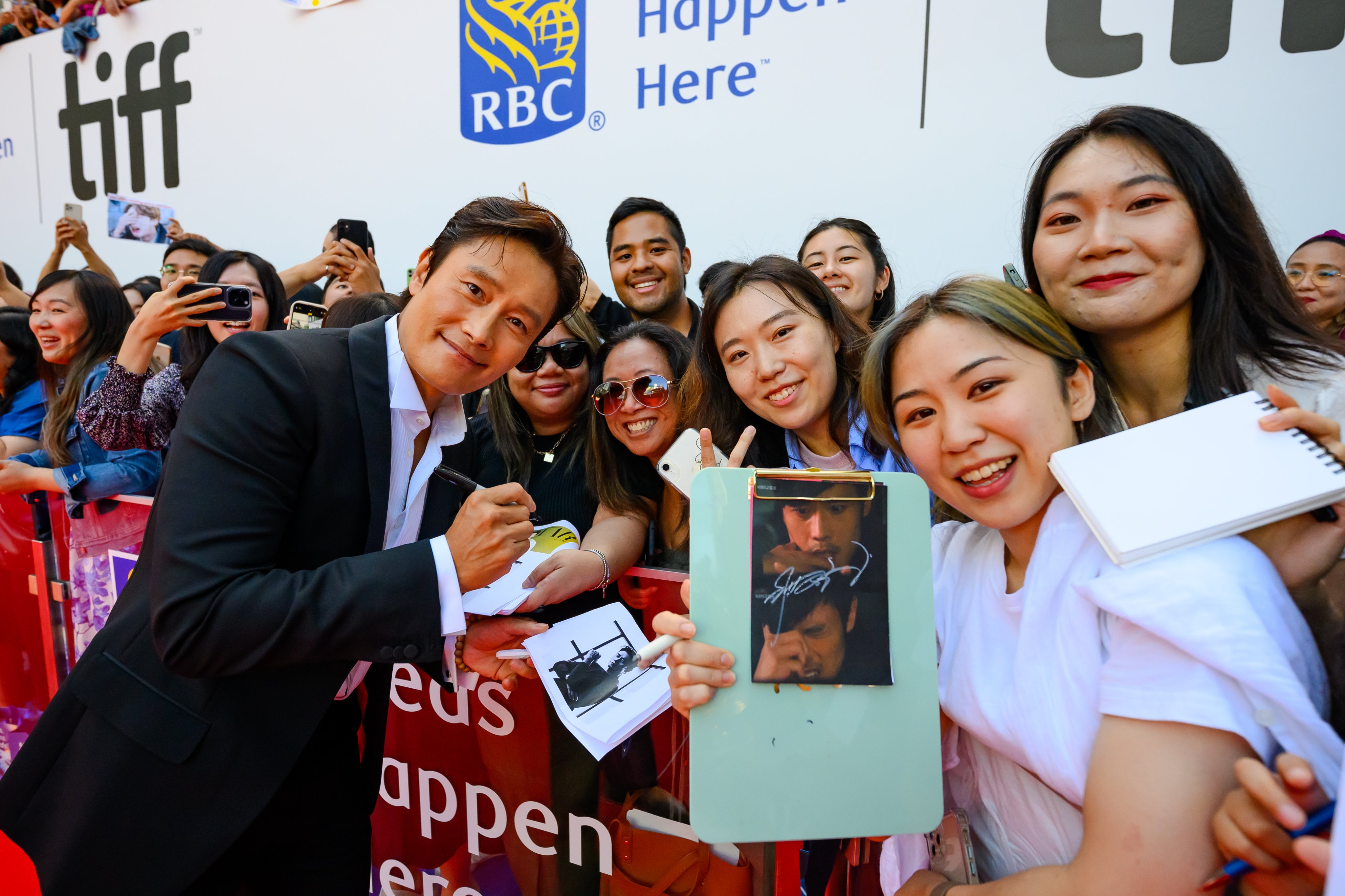 Lee Byung-hun smiling with fans as he is signing autographs. 
