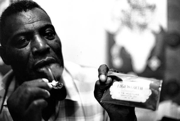 It's 1968 in San Francisco. Blues legend Howlin' Wolf is in a hotel room lighting his pipe. He's holding a package of Edgeworth Tobacco. (Photo by Sandy Guy Schoenfeld)