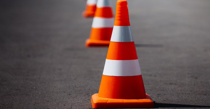 Top of an orange traffic cone with a white reflective stripe on it with a blurred background of a roadway.