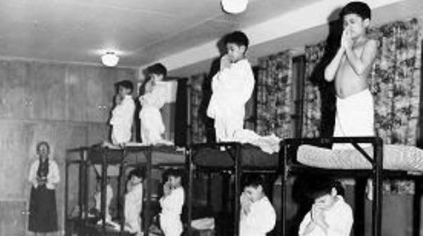 A creepy looking nun watch natives children in prayer. From 1880 to 1997 Canada forced indigenous children into residential schools to assimilate them into Canadian society. An estimated 6k to 25k died or went missing. Almost 2000 children have been found in unmarked, mass graves…