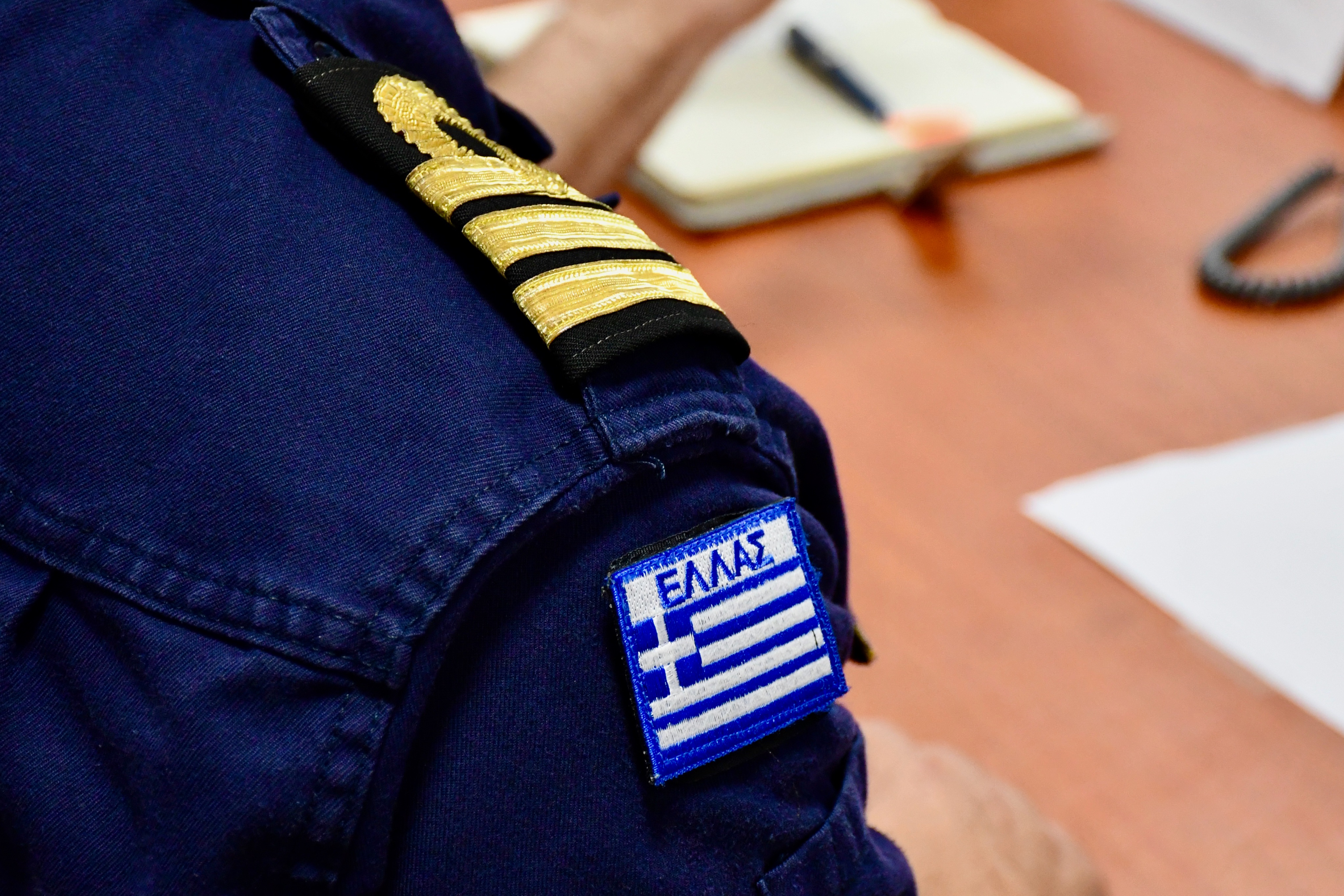 "Hellas" the Greek national flag and symbol of the Hellenic Navy on the uniform.