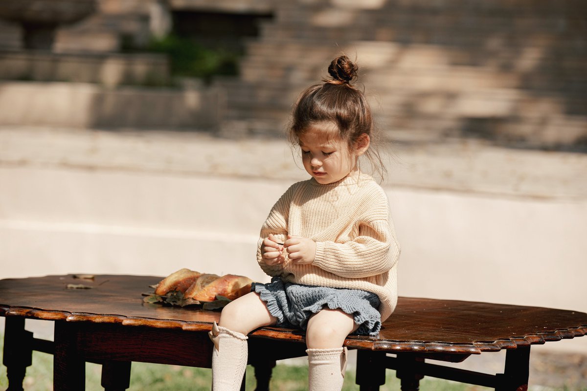 Serene Moments in the Great Outdoors ☀️🍂 Little girl, wrapped in a cozy sweater, sits quietly at the table. Surrounded by nature's play of light and shadows, she finds peace in the simple moments. 🌳🌿 #kaiyaangel #littlecontemplator #outdoorserenity